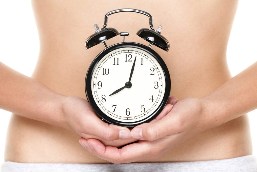 woman holding alarm clock in front of stomach