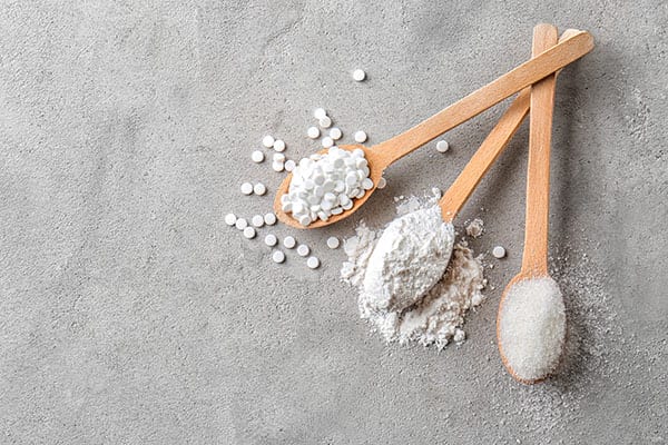 Wooden spoons with stevia pills, powdered and white sugar on grey table
